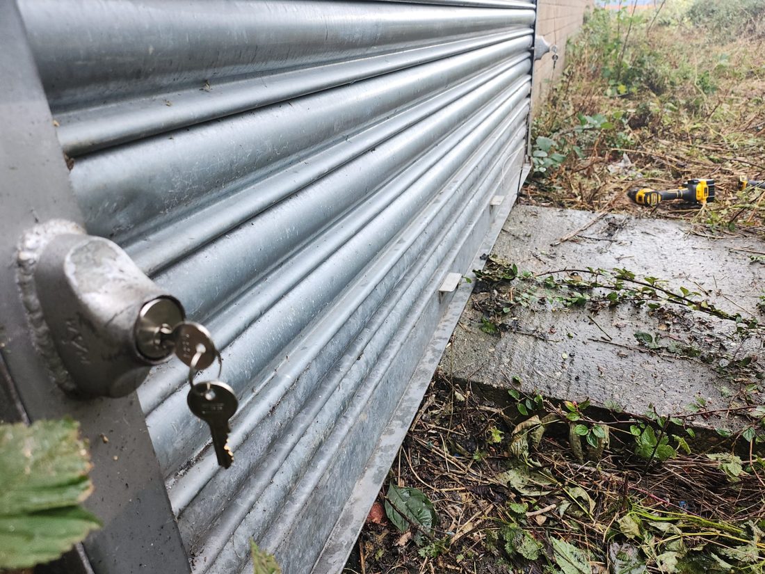 A bullet lock and keys fitted at the base of a galvanised steel roller shutter