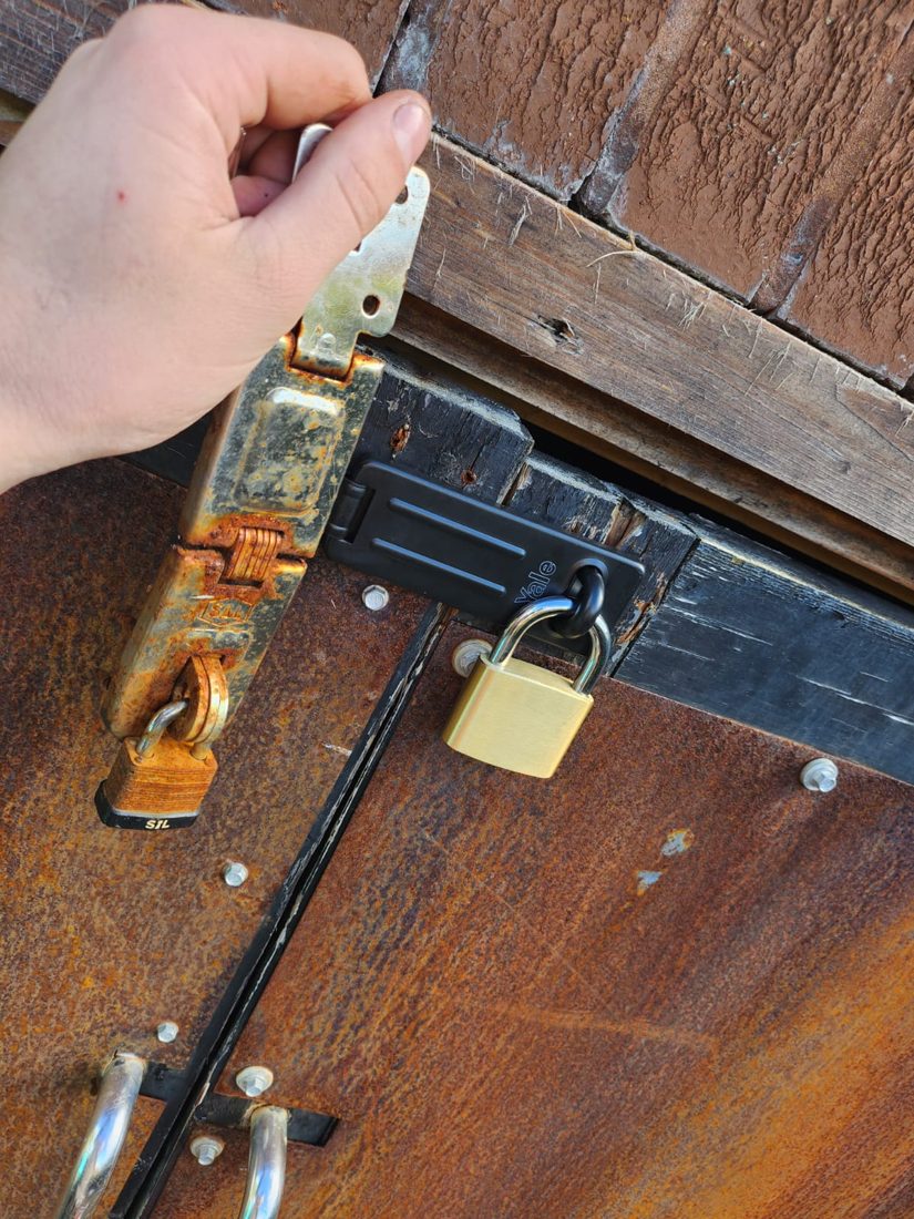 A hardened hasp and staple with a padlock fitted to a timber outbuilding door