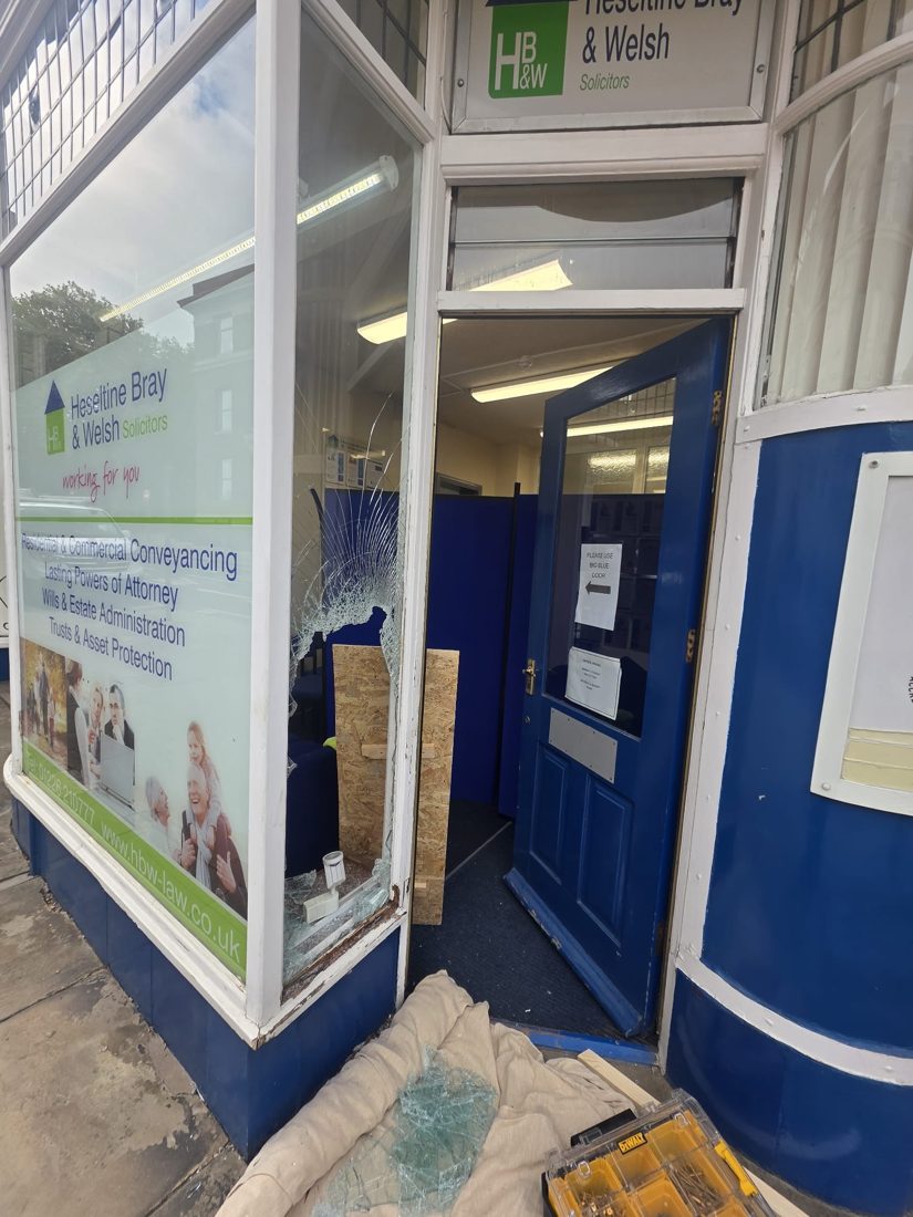 A solicitors' shop front with a smashed window being boarded and made secure