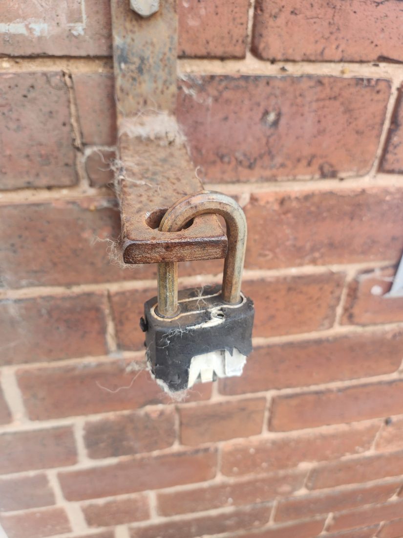 A padlock securing a metal gate against a brick wall
