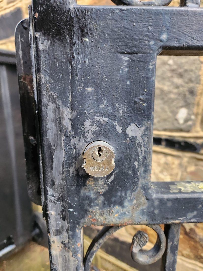 A replacement lock fitted to a black wrought-iron gate