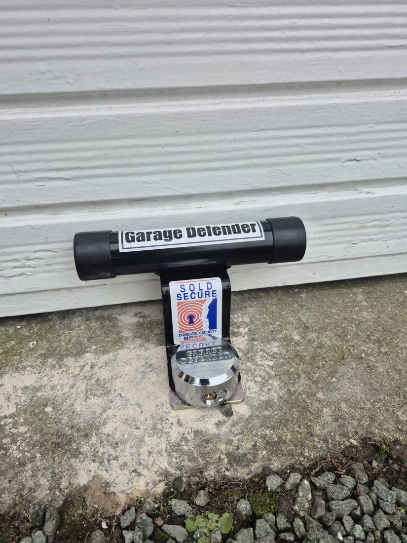 A Sold Secure garage defender ground-anchored at the base of an up-and-over garage door