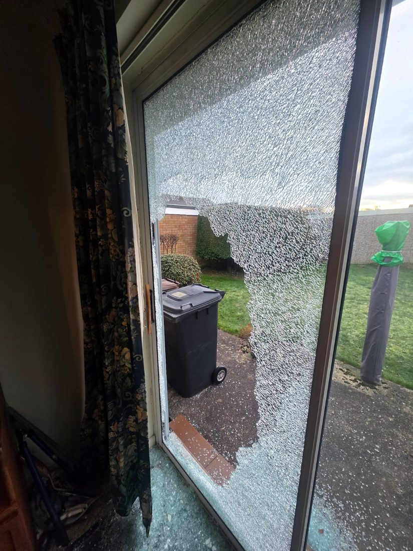 A smashed sliding patio door seen from inside, glass shattered across the floor, after an attempted break-in