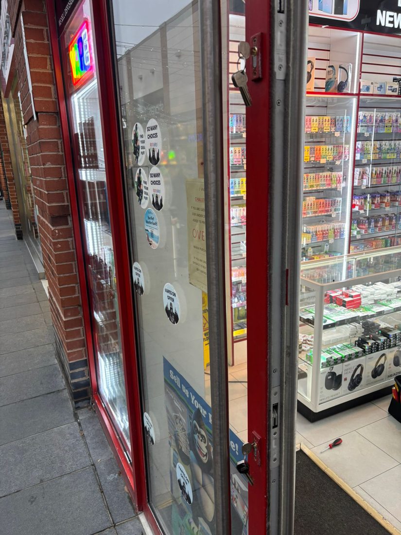 Two euro cylinders being changed on an open red-framed glass shopfront door