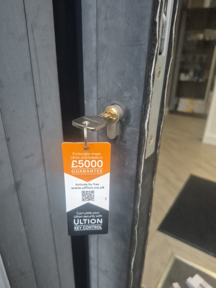 A euro cylinder with an Ultion key-control guarantee tag fitted to an aluminium shop door