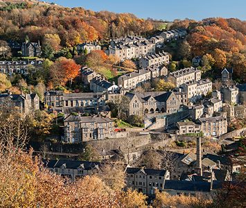 Stone terraced houses stacked up a steep wooded hillside in autumn — the characteristic layout of a Calder Valley township near Halifax