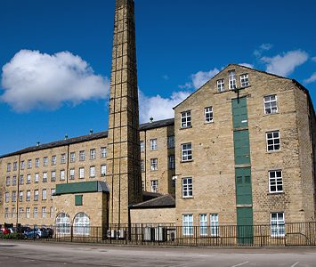 A large former textile mill with its tall chimney in Huddersfield, a surviving reminder of the town's woollen-industry heritage