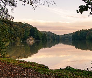 The lake at Newmiller Dam Country Park at dawn, the wooded shoreline reflected in the still water at the heart of the village